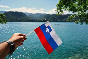 mão de homem segura a bandeira eslovena contra a vista do belo lago sangrado, eslovênia. foto