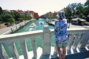 costas do menino ficam na ponte do canal com barcos em veneza, itália. foto