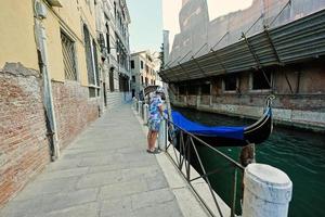 menino fica perto do canal com gôndola coberta em veneza, itália. foto