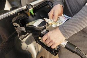 carro reabastecimento no posto de gasolina. homem reabastecendo o carro com combustível e segurando dinheiro, euros. fechar-se. gasolina, o diesel está ficando mais caro. indústria petrolífera e serviços. preço da gasolina e crise do petróleo. foto