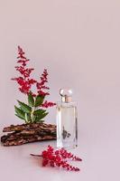 um frasco de perfume feminino ou água de toalete em um fundo rosa com flores e casca de uma árvore. apresentação do aroma de um cheiro natural. foto