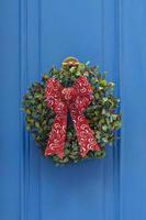 tradicional guirlanda de natal verde e vermelha pendurada na porta de entrada azul da casa. decoração de casa tradicional durante o natal foto