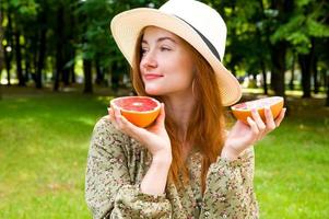 jovem mulher ruiva feliz em um chapéu segurando toranja. conceito de retrato de verão. frutas e vitaminas foto