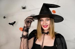 elegante bruxa de halloween contra fundo assustador com aranhas, teia e apostas câmera sorridente. 31 de outubro festa doces ou travessuras foto