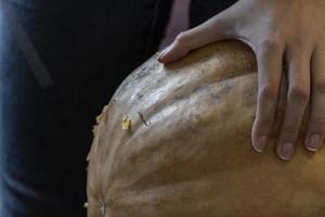 fêmea esculpindo grande abóbora laranja para o halloween enquanto está sentado na mesa de madeira em casa foto