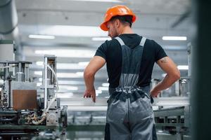 pegando a janela. trabalhador industrial dentro de casa na fábrica. jovem técnico com capacete laranja foto