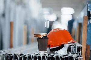 pão está no copo com bebida. capacete laranja em objetos na fábrica. ninguém. concepção da pausa para o almoço foto