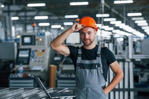 tocando capacete de proteção. trabalhador industrial dentro de casa na fábrica. jovem técnico com capacete laranja foto