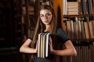 detém muitos livros nas mãos. aluna está na biblioteca. concepção de educação foto