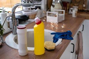 limpando a cozinha antes dos feriados de natal e ano novo. detergente, pó seco, esponja, luvas estão na pia. decoração festiva na cozinha branca, interior aconchegante da casa foto