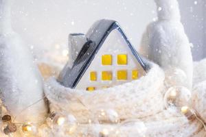 casa aconchegante está embrulhada em um chapéu e cachecol em uma decoração de peitoril da janela de tempestade de neve. inverno, neve - isolamento doméstico, proteção contra o frio e o mau tempo, sistema de aquecimento do ambiente. clima festivo, natal, ano novo foto