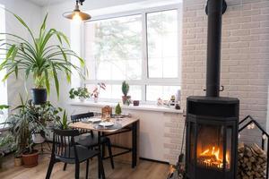 interior festivo da casa é decorado para o natal e ano novo em estilo loft com fogão preto, lareira, árvore de natal. sala de estúdio quente com cozinha branca, queima de madeira, aconchegante e aquecimento de casa foto