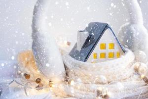 casa aconchegante está embrulhada em um chapéu e cachecol em uma decoração de peitoril da janela de tempestade de neve. inverno, neve - isolamento doméstico, proteção contra o frio e o mau tempo, sistema de aquecimento do ambiente. clima festivo, natal, ano novo foto