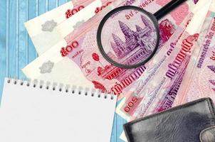 500 contas de riels cambojanos e lupa com bolsa preta e bloco de notas. conceito de dinheiro falso. procurar diferenças em detalhes em notas de dinheiro para detectar falsificações foto