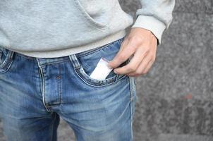 mão masculina recuperando o pacote de drogas do bolso de jean azul com espaço de cópia no fundo do prédio abandonado foto