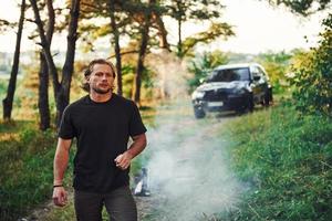 retrato do homem que fica na floresta e olha para a natureza. automóvel estacionado atrás foto