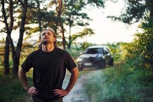 automóvel preto atrás. retrato do homem que fica na floresta e olha para a natureza foto