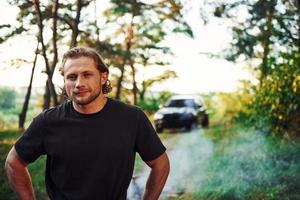 retrato do homem que fica na floresta e olha para a natureza. automóvel estacionado atrás foto