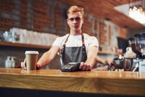 tome sua bebida por favor. trabalhador de café masculino jovem dentro de casa. concepção de negócio e serviço foto