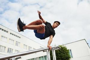 grades prateadas. jovem esportista fazendo parkour na cidade durante o dia ensolarado foto