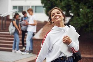 Garota alegre. grupo de jovens estudantes em roupas casuais perto da universidade durante o dia foto