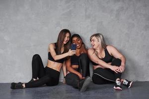 usando smartphone. grupo de mulheres multiétnicas sentadas no estúdio contra um fundo cinza foto