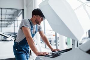 decidir o que fazer primeiro. homem de uniforme azul e chapéu preto, reparando o automóvel danificado foto