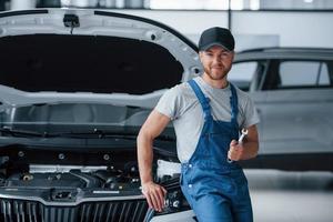 vamos consertar qualquer coisa. funcionário de uniforme de cor azul fica no salão de automóveis foto