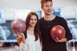 casal feliz segurando bolas de boliche nas mãos e se divertir no clube foto