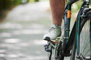 pé no pedal. ciclista de bicicleta está na estrada de asfalto na floresta em dia ensolarado foto