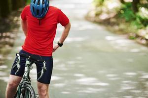 preparando-se para um passeio. ciclista de bicicleta está na estrada de asfalto na floresta em dia ensolarado foto