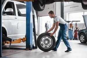 pneu novo. funcionário de uniforme de cor azul trabalha no salão de automóveis foto