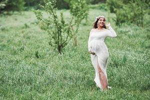 sons agradáveis da natureza. linda mulher grávida de vestido dar um passeio ao ar livre. morena positiva foto