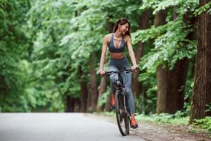 com sorriso no rosto. ciclista feminina em uma bicicleta na estrada de asfalto na floresta durante o dia foto