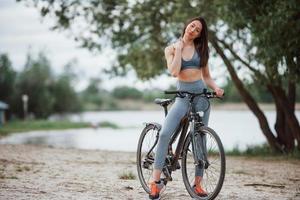 eu amo esse lugar. ciclista feminina com boa forma corporal em pé com sua bicicleta na praia durante o dia foto