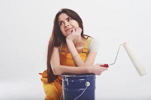 olhar sonhador. mulher morena de uniforme amarelo senta-se contra um fundo branco no estúdio foto