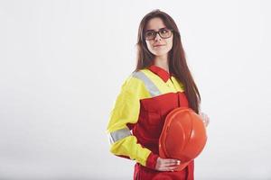 capacete protetor nas mãos. mulher morena de uniforme laranja e amarelo fica contra um fundo branco no estúdio foto