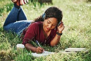 aluno faz lição de casa ao ar livre. alegre mulher afro-americana no parque no verão foto