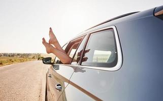 na estrada. menina põe as pernas para fora na janela do automóvel na zona rural foto