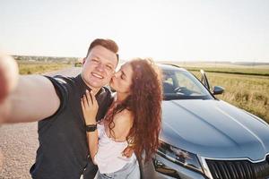 cara segura a câmera. lindo casal perto de seu novo carro moderno no fim de semana foto