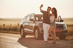 luz solar incrível. lindo casal perto de seu novo carro moderno no fim de semana foto