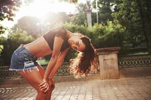 sol sobre o corpo. mulher bonita com cabelo preto encaracolado se diverte na cidade durante o dia foto