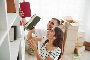 cada livro deve estar em seu lugar certo. casal jovem alegre em seu novo apartamento. concepção de movimento foto