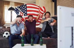 três amigos animados assistindo futebol na tv em casa juntos foto