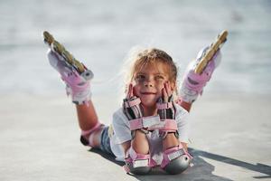 deitado. menina bonitinha com patins ao ar livre perto do lago no fundo foto