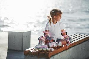menina bonitinha com patins ao ar livre perto do lago no fundo foto