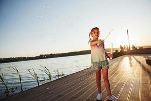 tempo da noite. menina feliz brincando com bolhas perto do lago no parque foto