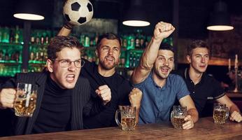 com bola de futebol. é uma meta. comemorando a vitória. três fãs de esportes em um bar assistindo futebol com cerveja nas mãos foto