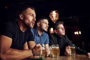 três fãs de esportes em um bar assistindo futebol. com cerveja nas mãos foto