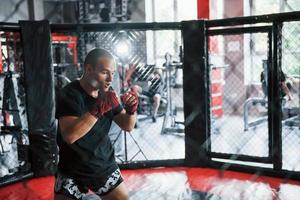 jovem boxeador em bandagens vermelhas tem exercício. no ginásio na jaula foto